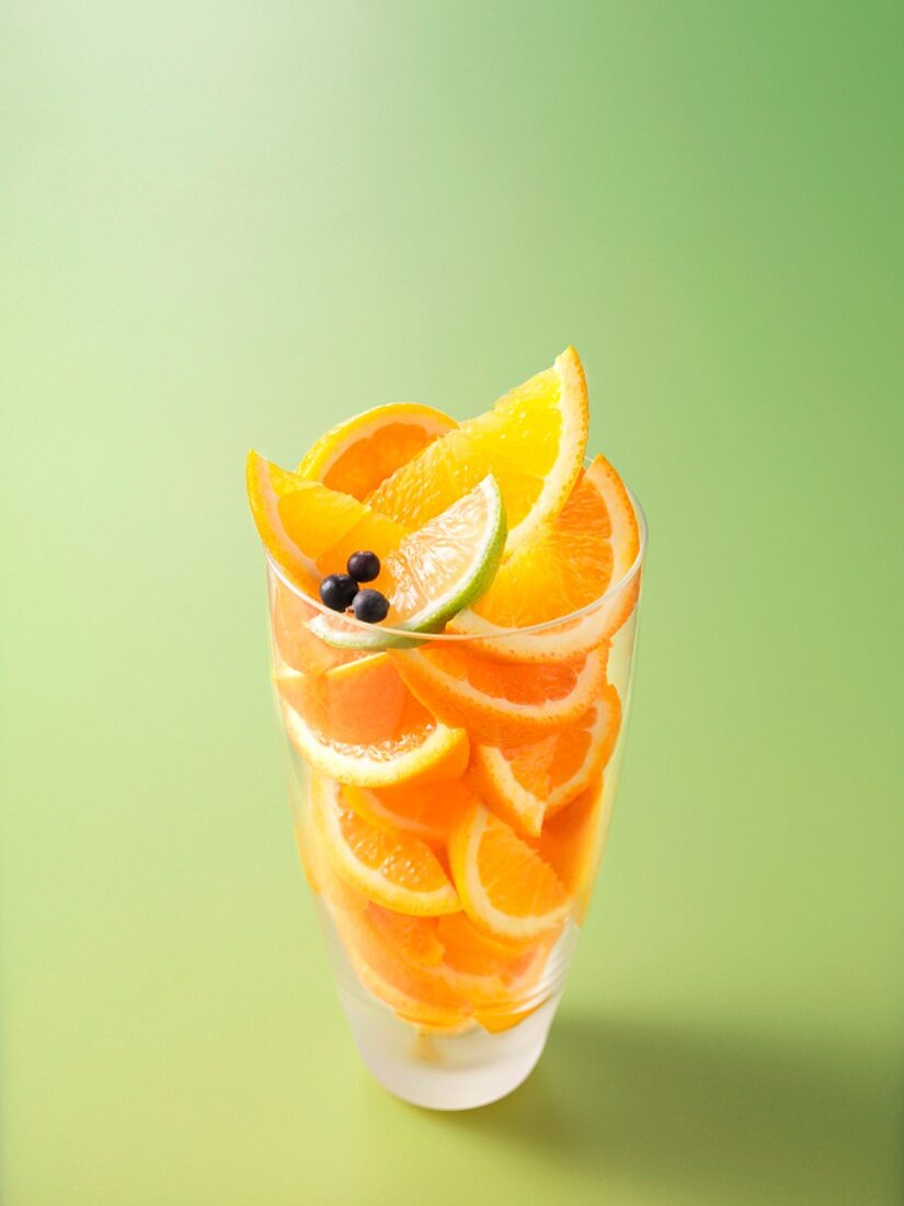 Zutaten für einen Fruchtsaft mit Orange, Limette und Wacholderbeeren im Glas