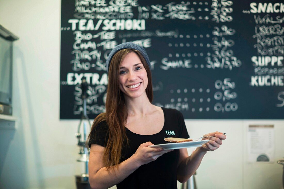 A young waitress with a plate of cake standing in front of a menu board