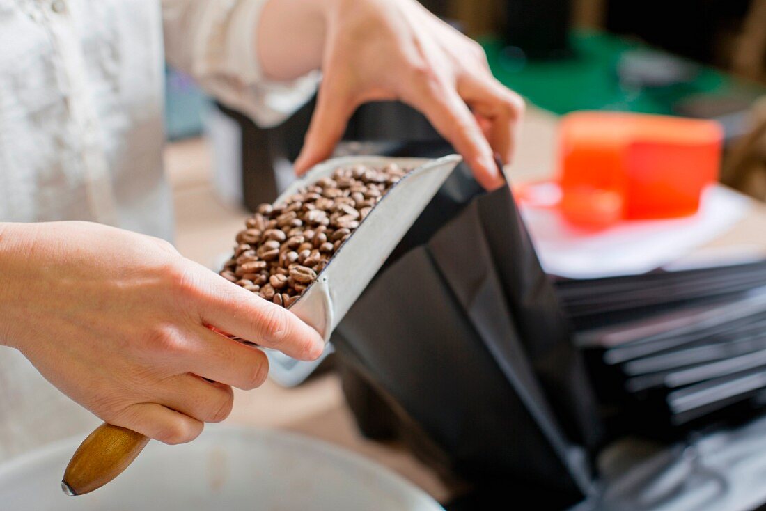 Frau füllt Kaffeebohnen in eine schwarze Papiertüte