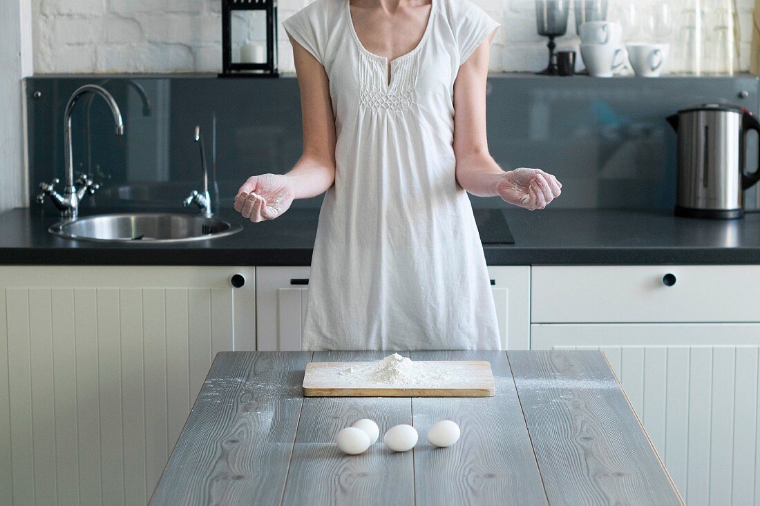 A woman with flour on her hands standing at a kitchen table