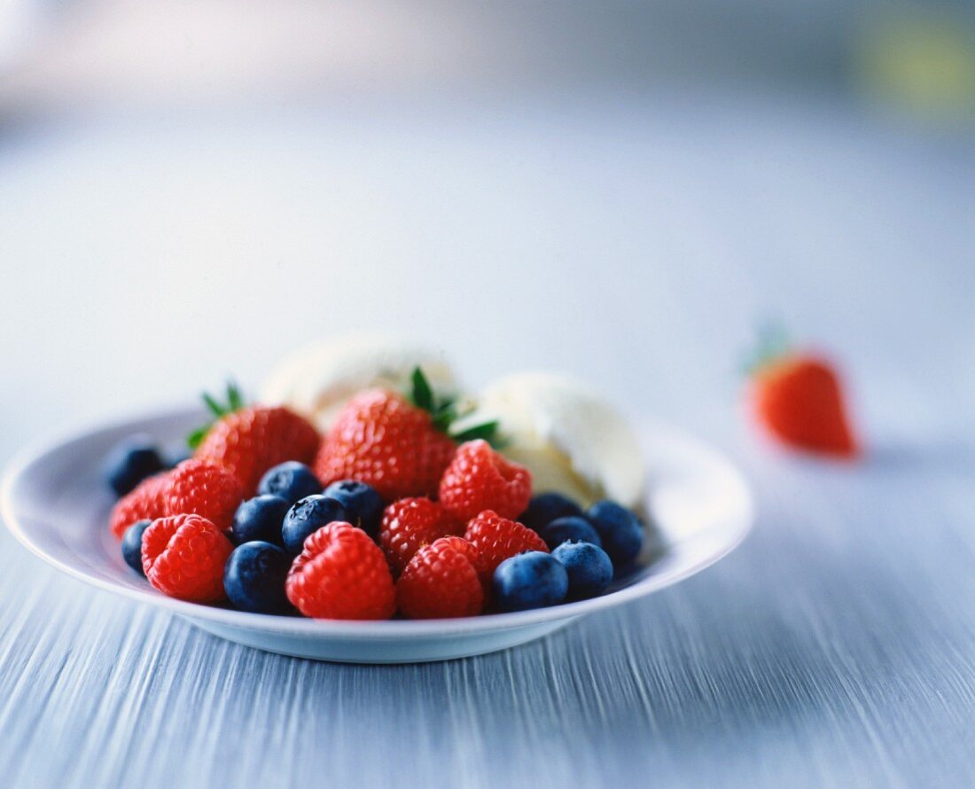 Raspberries, strawberries, blueberries and vanilla ice cream on white plate