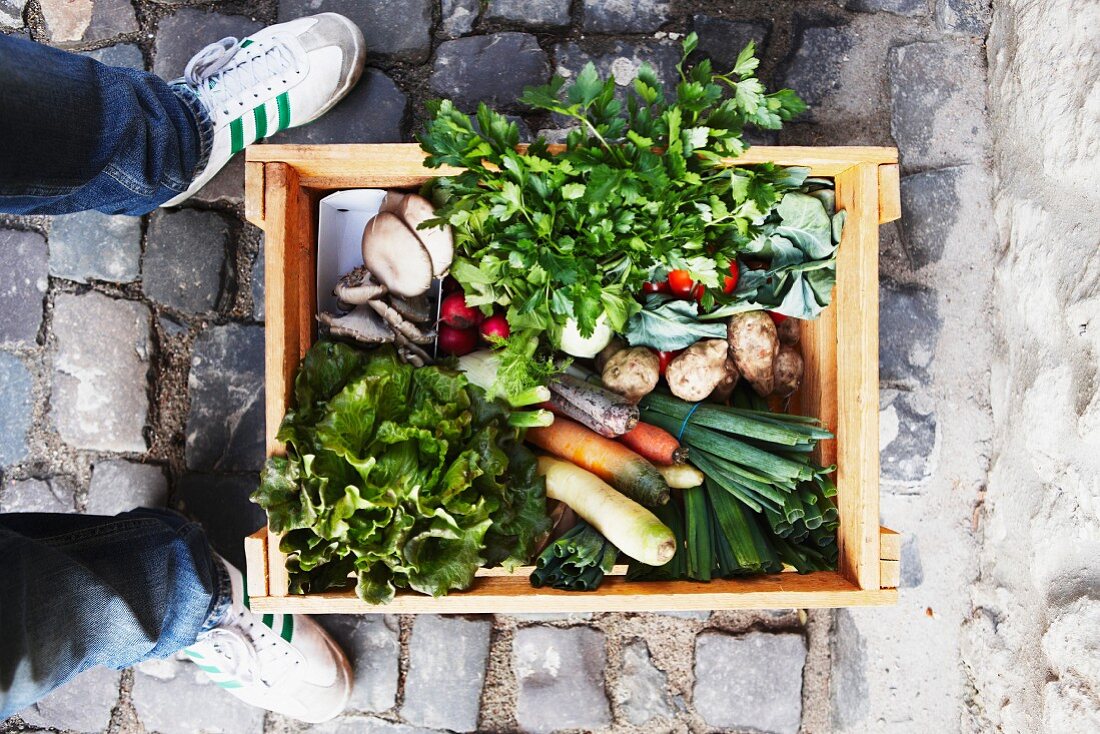 A person standing next to a crate of vegetables on cobble stones