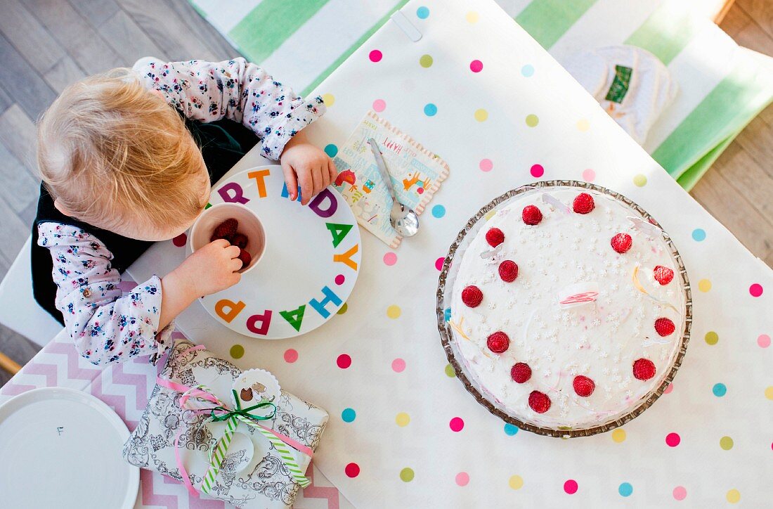 Small child sitting at a table with a birthday cake (seen from above)
