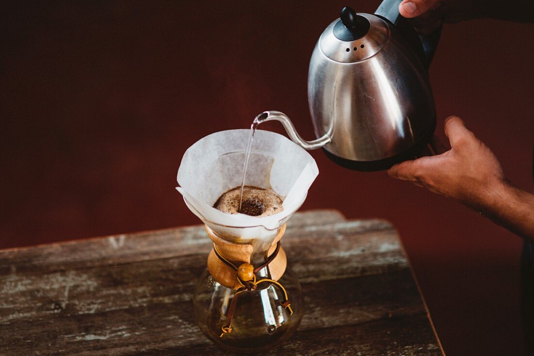 Person pouring water through a coffee filter in a Chemex coffee carafe
