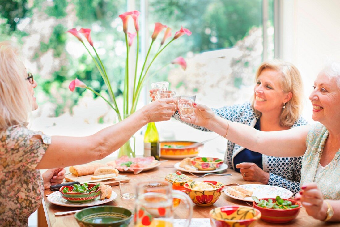 Drei ältere Damen beim gemeinsamen Essen und Anstossen mit Getränken