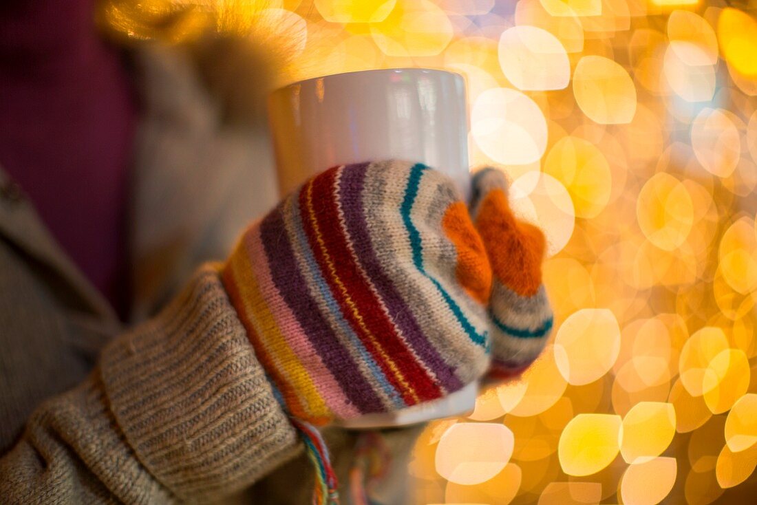 Frauenhände mit Handschuhen halten Heissgetränk vor Weihnachtsbeleuchtung