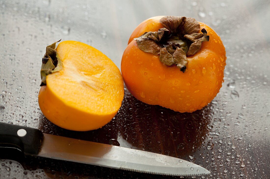 Persimmons, whole and halved, sprayed with water drops