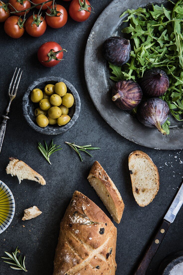 Frisches Brot, Oliven, Tomaten, Salat, Feigen und Olivenöl auf grauem Tisch