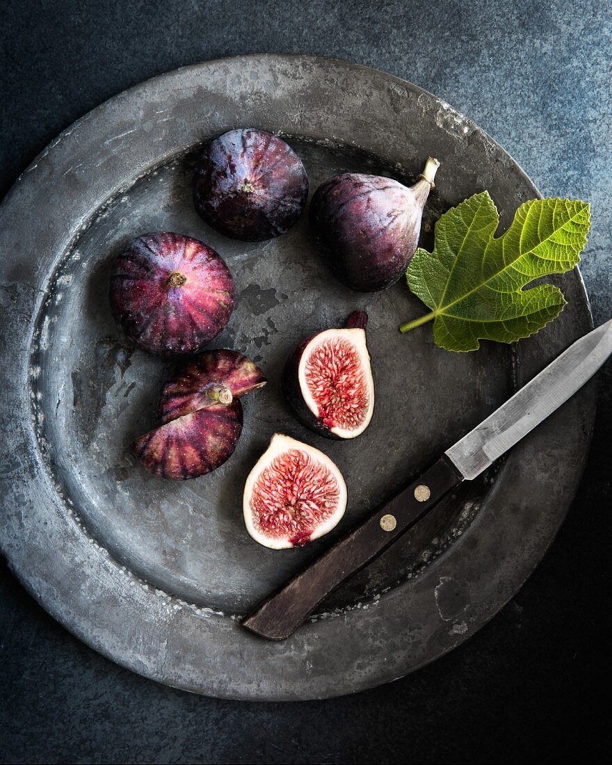 Fresh figs on a metal plate with a knife and a fig leaf (seen from above)