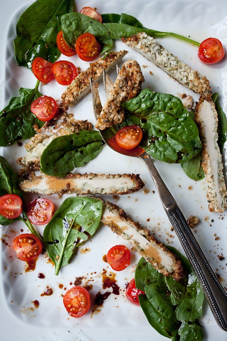 Breaded chicken goujons with spinach and tomatoes drizzled with olive oil and balsamic vinegar