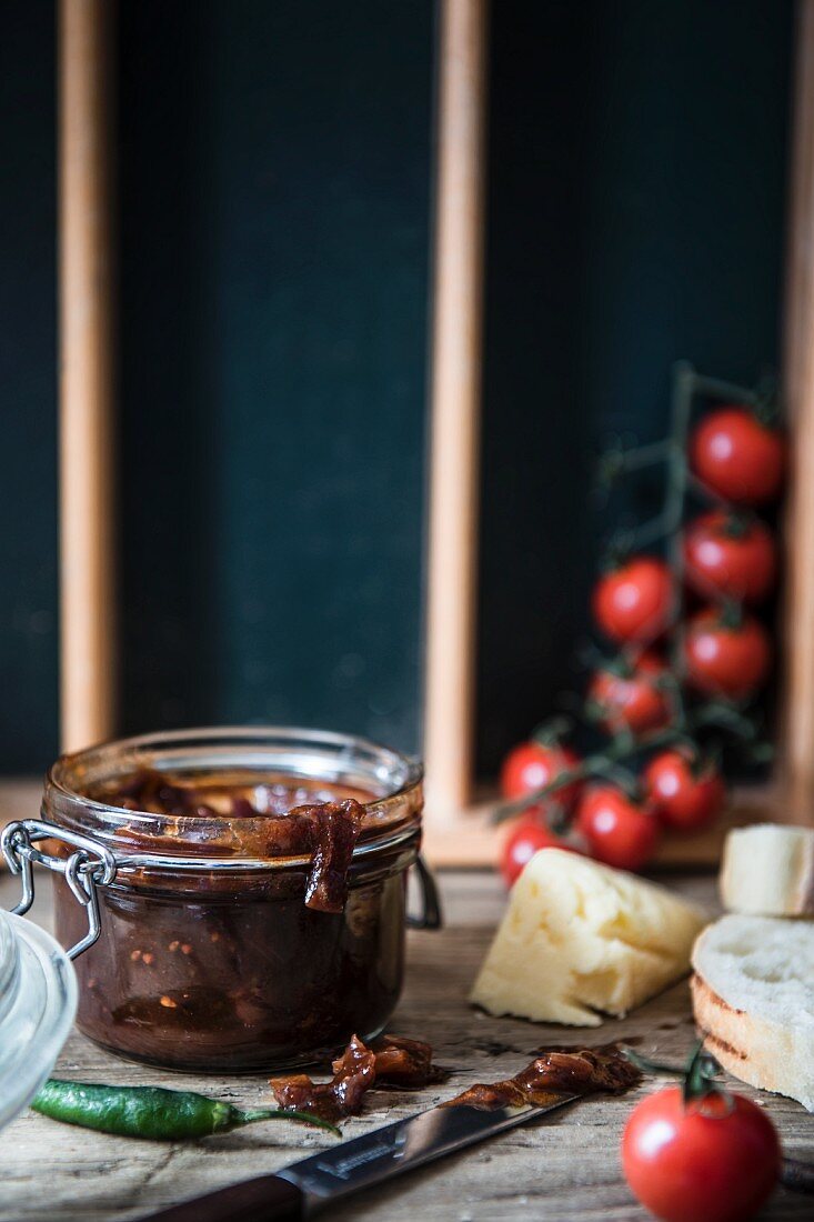 A jar of chutney with bread, cheese, cherry tomatoes and a chilli pepper