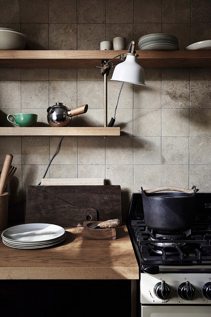 Kitchenette with wooden worktop and wall shelves in front of tiled wall, gas stove next to it