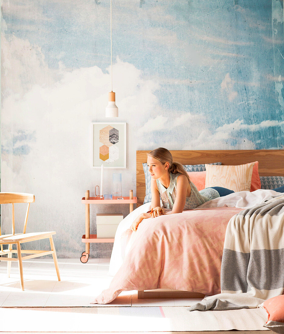 Junge Frau auf Doppelbett vor Studiowand mit Himmelmotiv