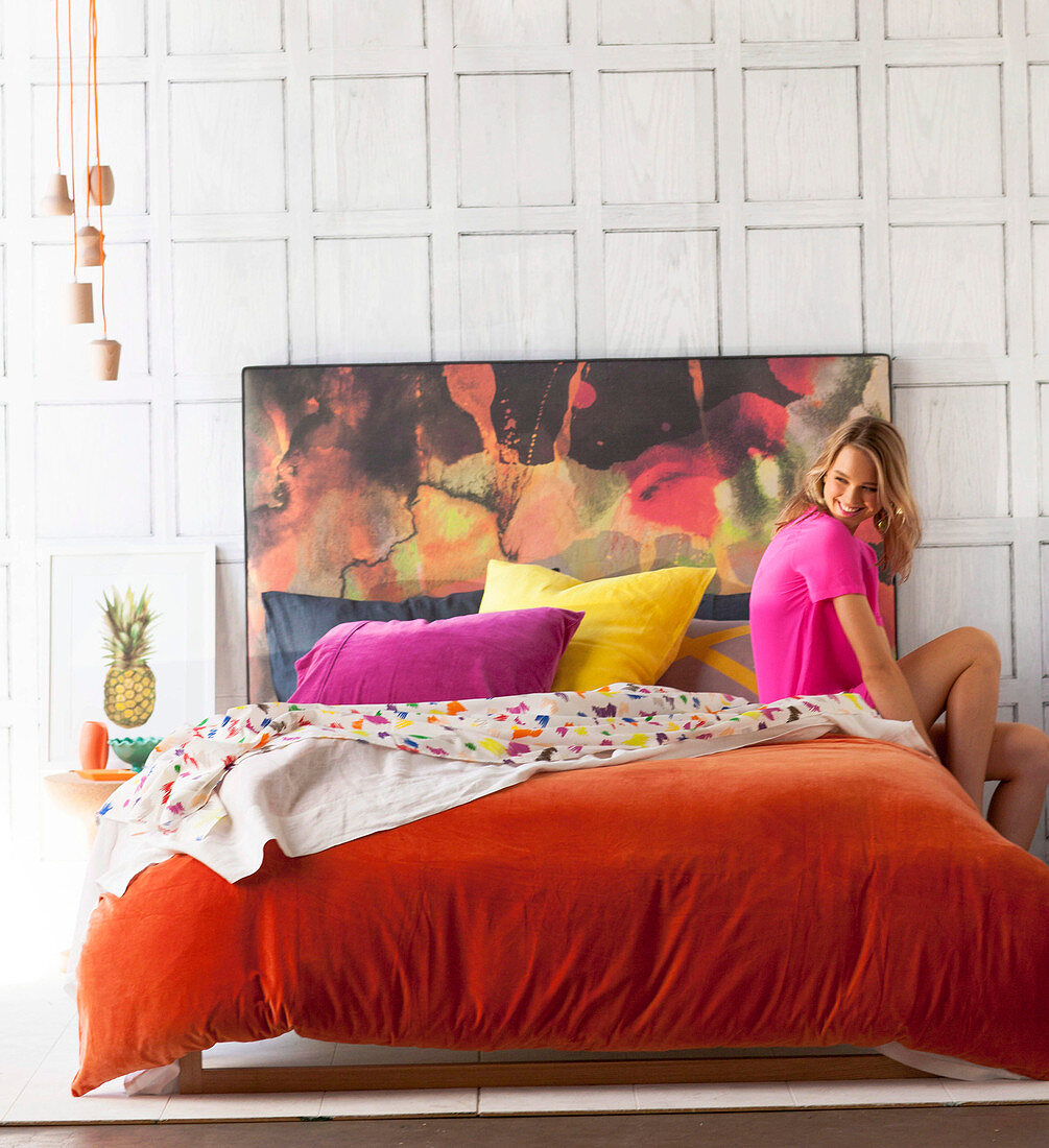 Young woman on double bed with orange velvet cover and colorful headboard