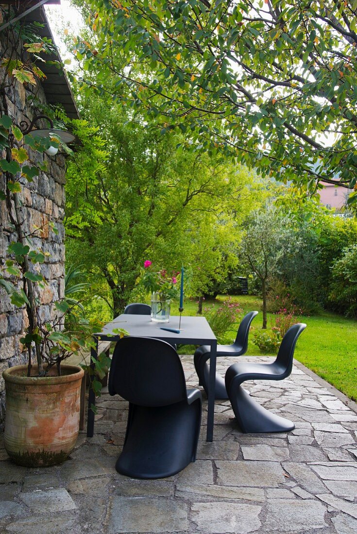 Outdoor Essplatz mit schwarzen Klassiker-Schalenstühlen auf Natursteinboden vor Rustiko