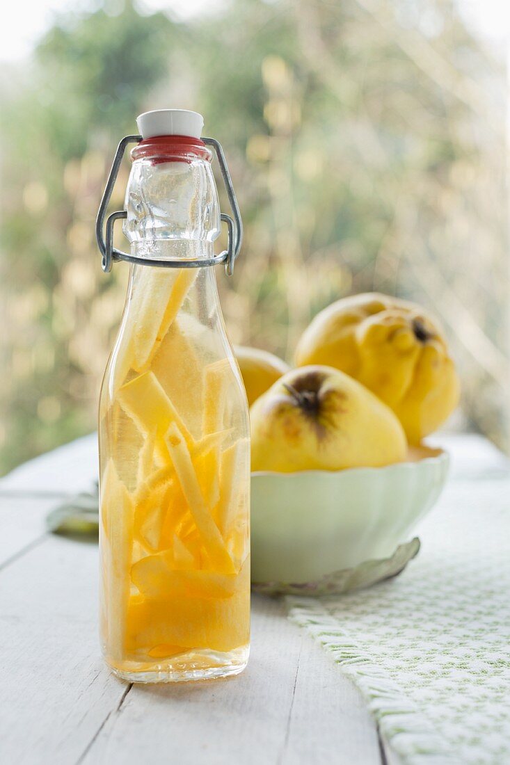 Quince schnapps in a bottle, with fresh quinces in a vintage bowl in the background