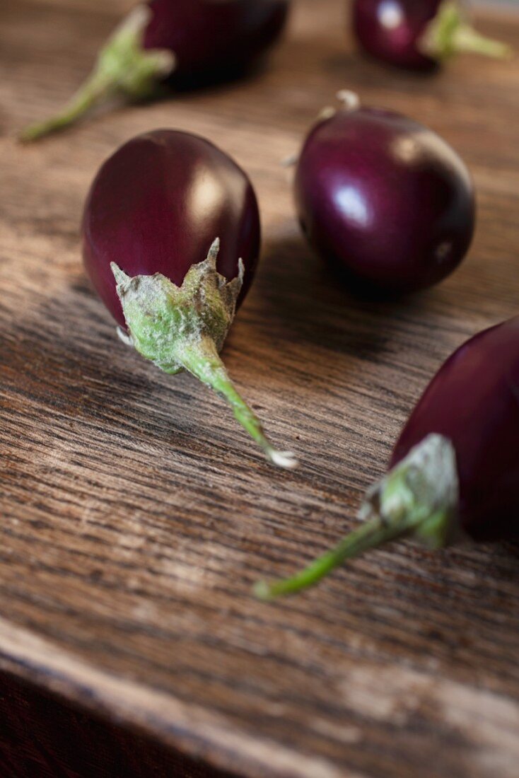 Five fresh purple aubergines on a wooden surface