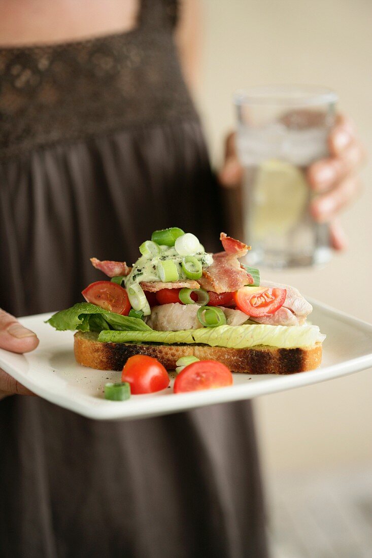 Frau hält Teller mit Chicken Club Salad auf Röstbrot