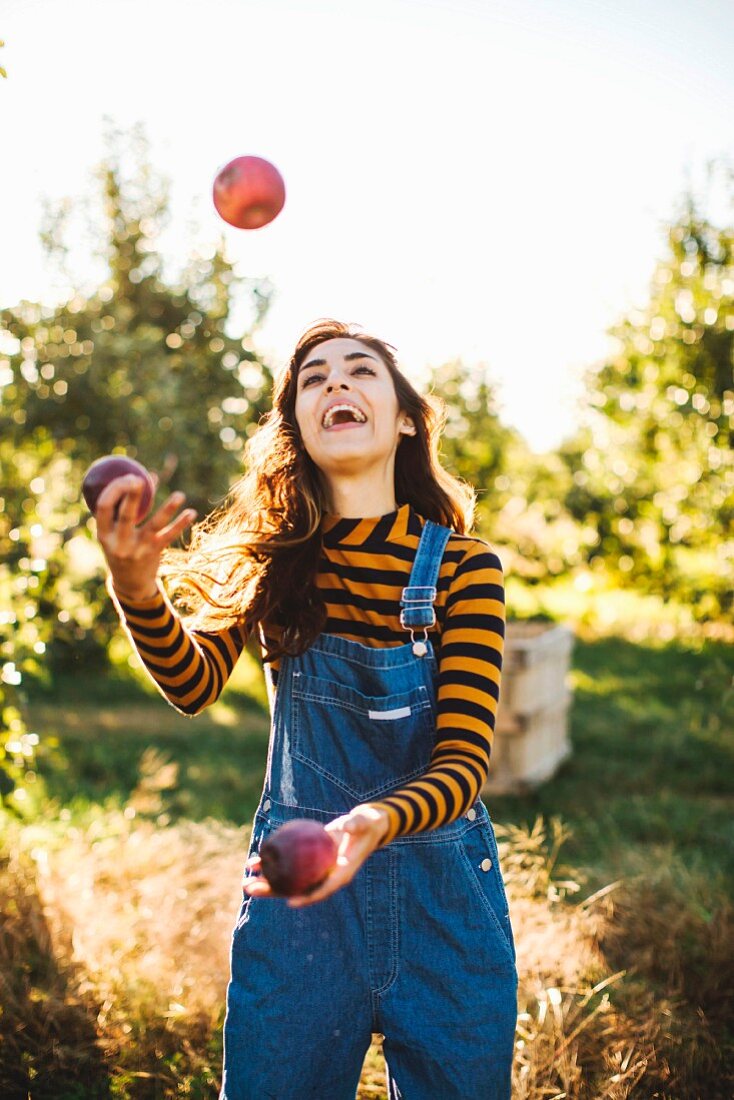 A young woman wearing dungarees juggling with apples