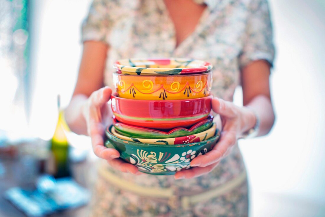 A woman holding a stack of colourful ceramic bowls