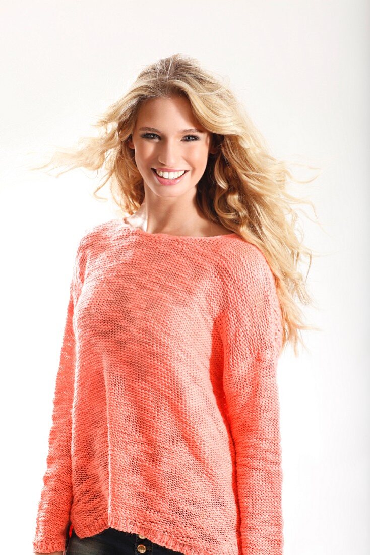 A young blonde woman wearing a knitted salmon coloured jumper