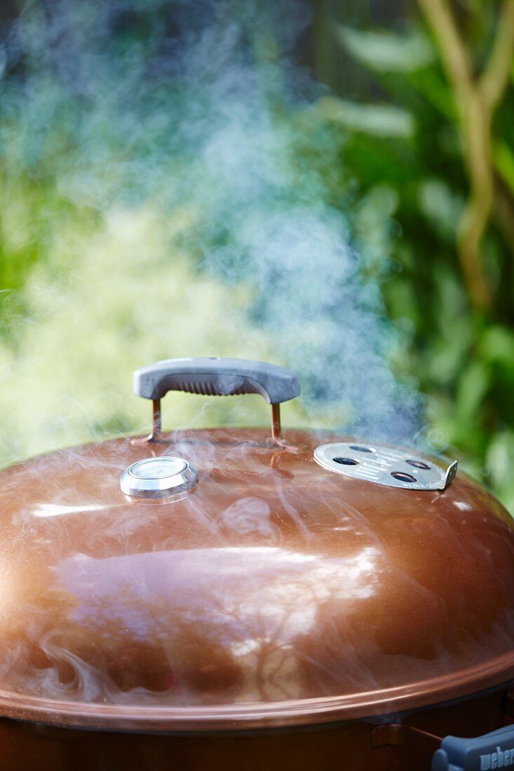 A smoking kettle barbecue in a garden
