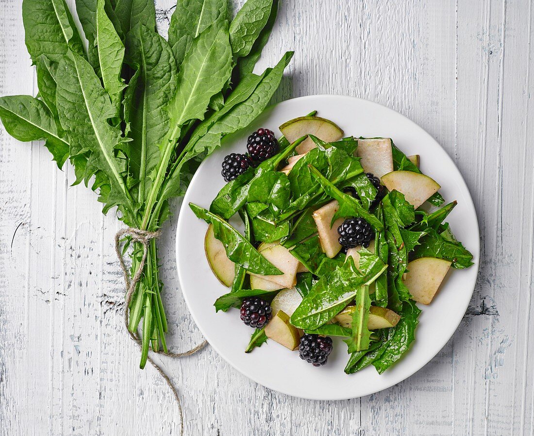 Dandelion salad with pears and blackberries on white wooden table