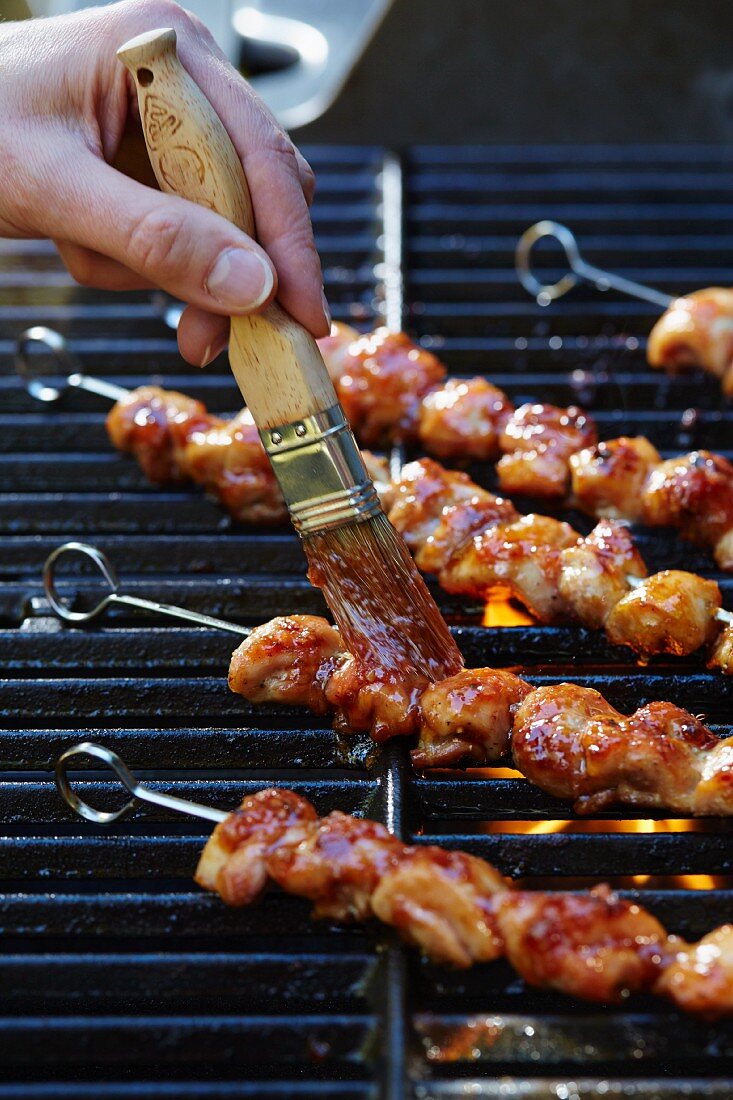 Chicken skewers on a barbecue being brushed with a Thai chilli marinade