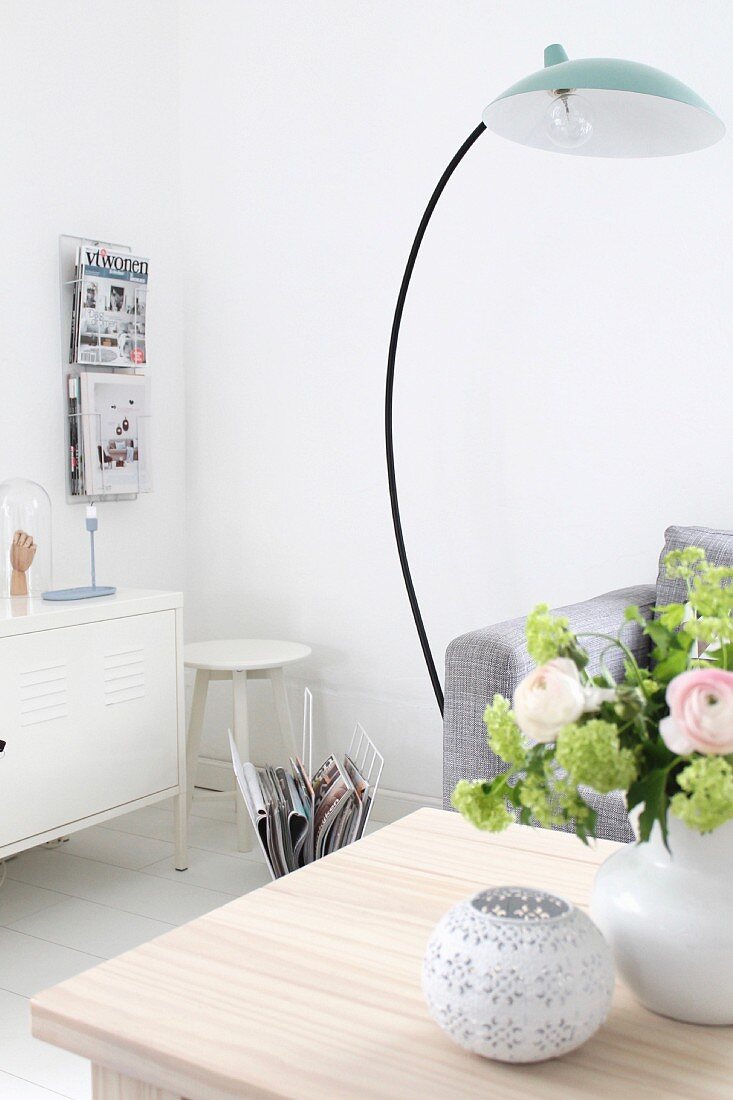Wohnbereich mit Bogenlampe und Blumenstrauss auf Couchtisch vor weißem Metall Sideboard und Zeitschriftenhalter