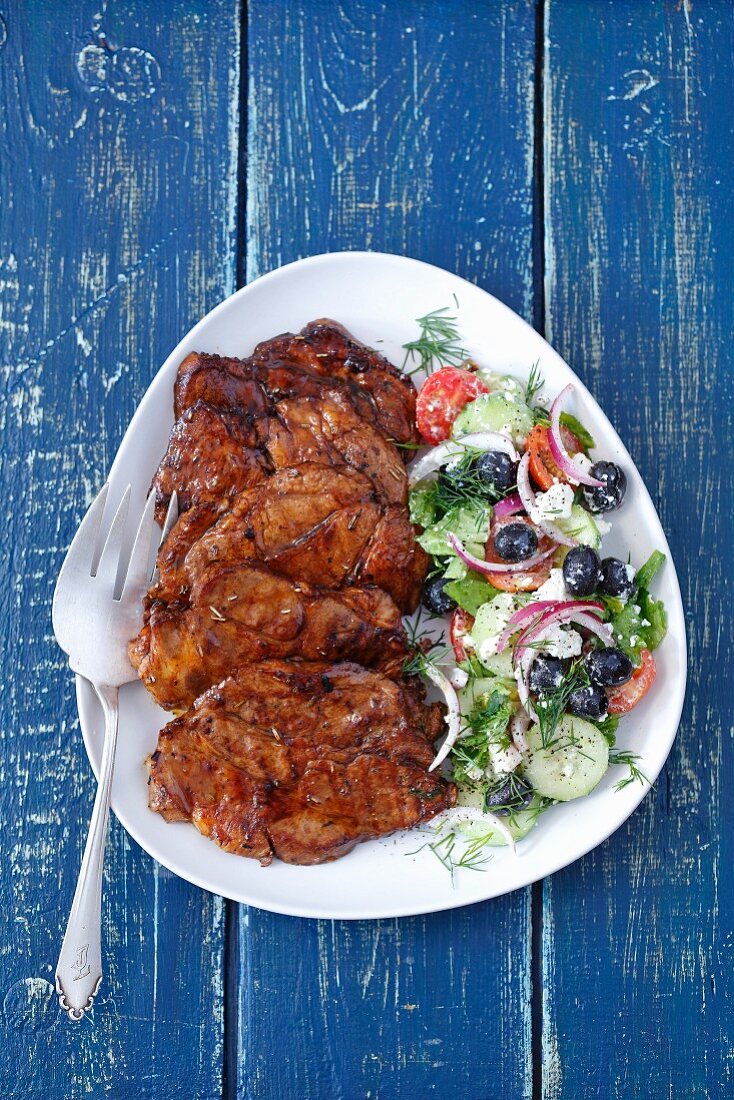 Grilled pork collar served with salad with black olives, tomatoes and feta cheese