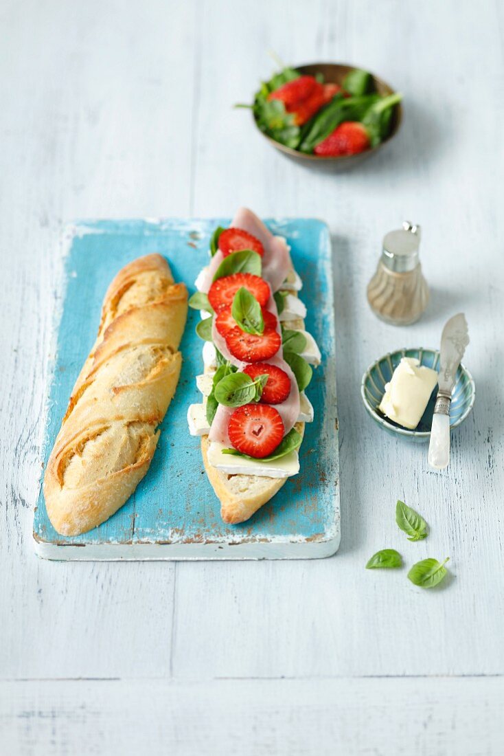 A baguette sandwich with spinach, basil, ham, Camembert and strawberries