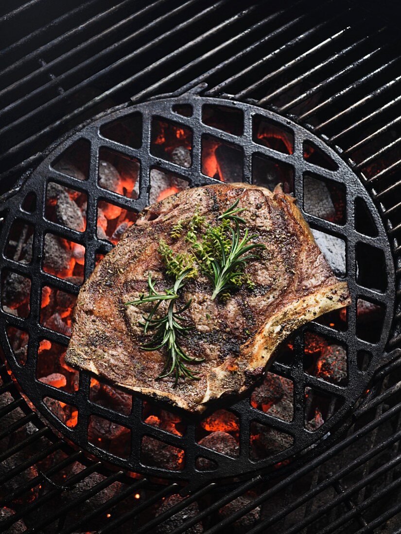 A rib-eye steak with herbs on a barbecue