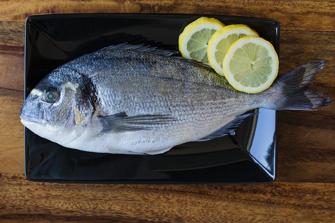 Seabream with lemon slices on a black plate (ingredients for seabream in a salt crust)