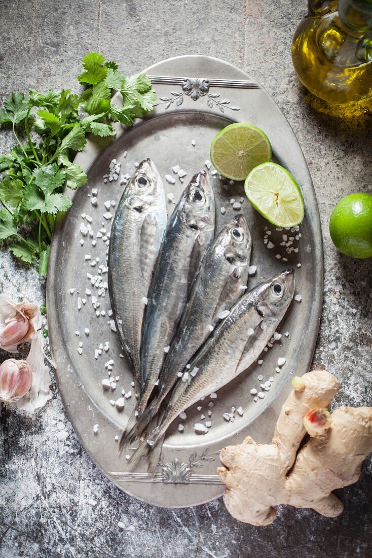 Raw sardines on a silver tray with ingredients