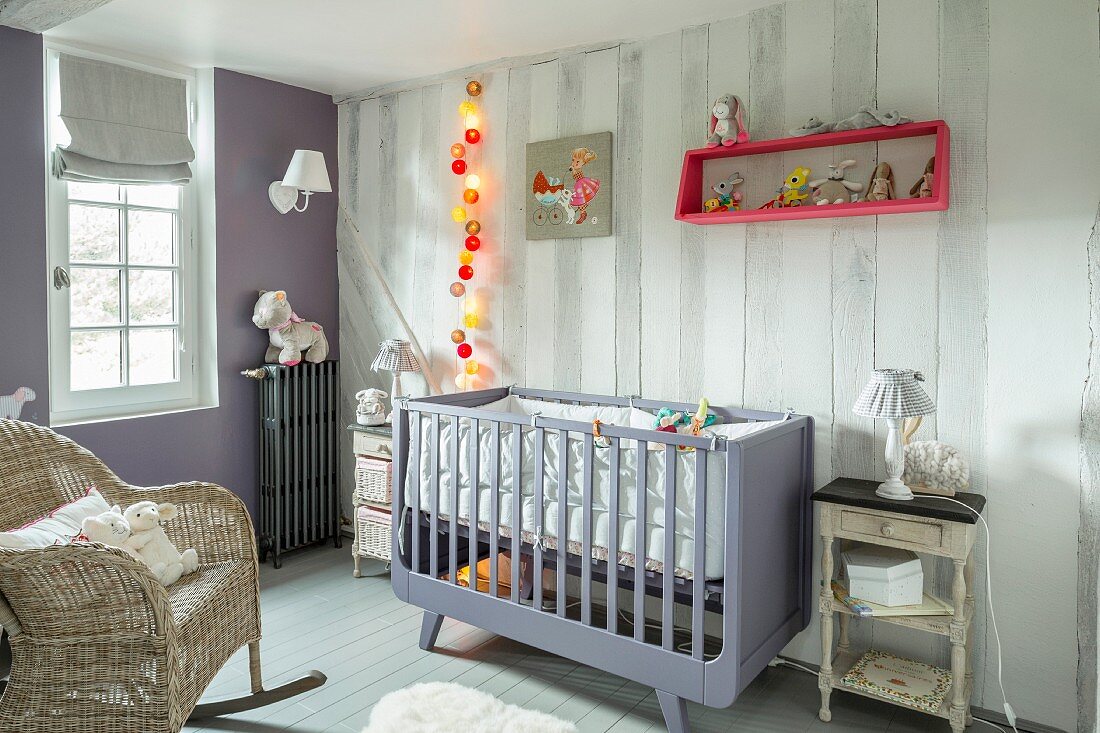Cot, wicker rocking chair and lit fairy lights in vintage-style nursery