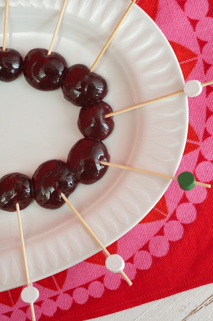 Cherries stuck on decorated wooden skewers on white plate
