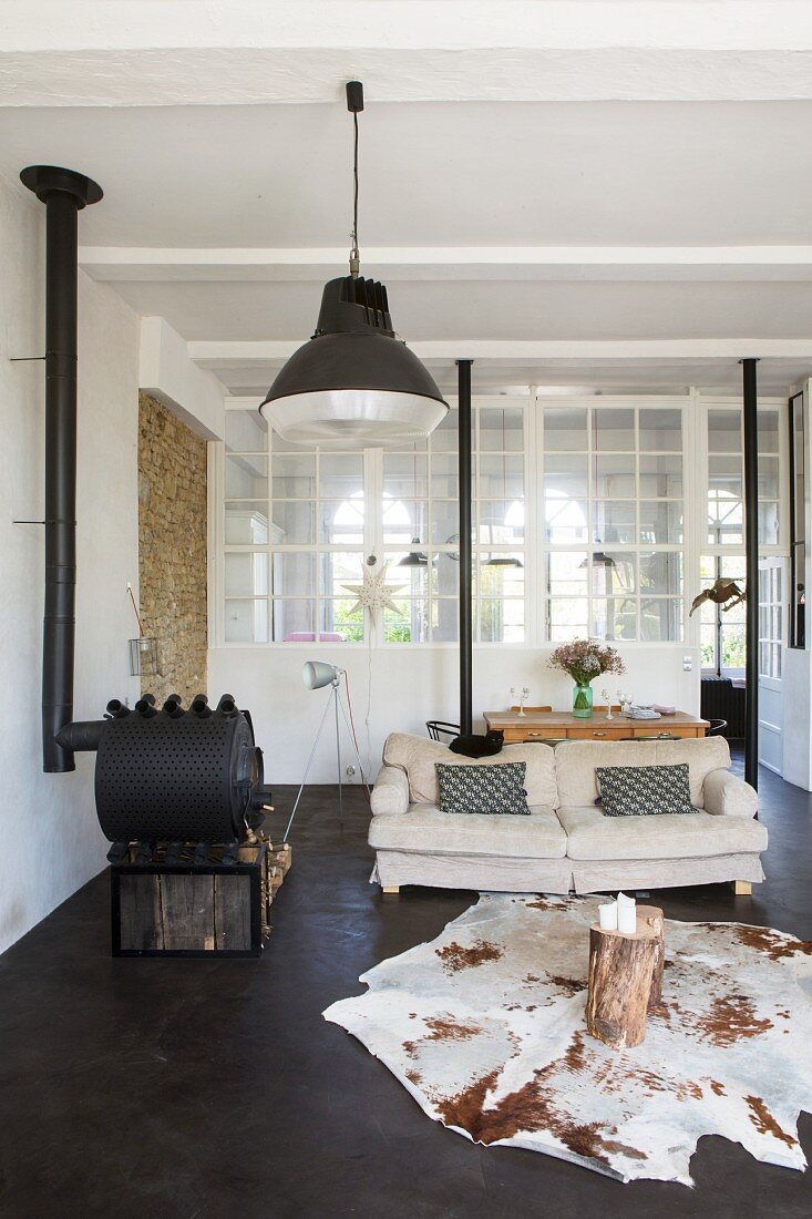 Loungebereich mit Tierfellteppich, Baumstumpf-Tisch und Kaminofen vor Innenfenster
