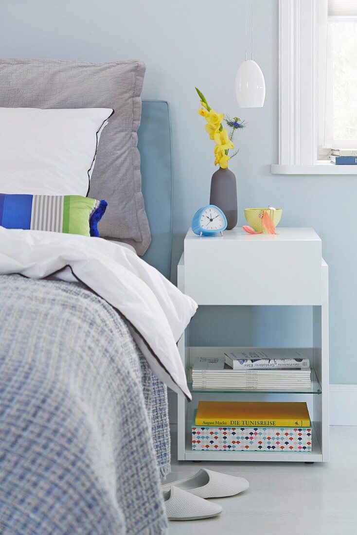 A white bedside table next to a box spring bed