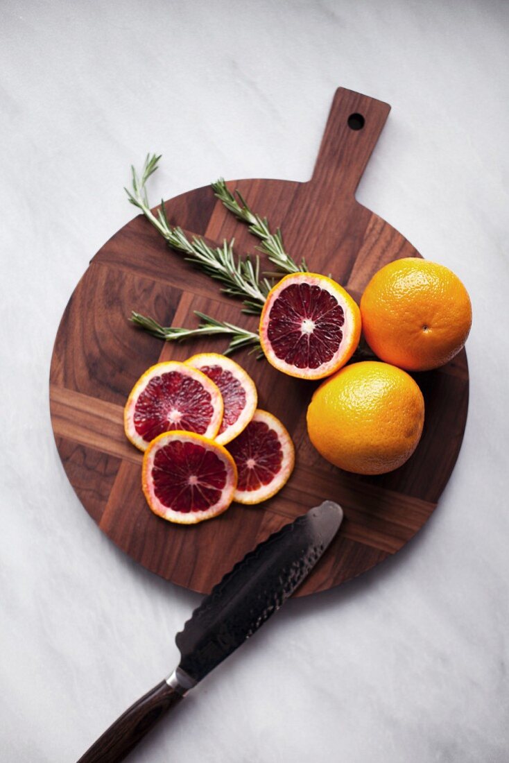 Blood oranges, whole and sliced on a wooden chopping board (seen from above)