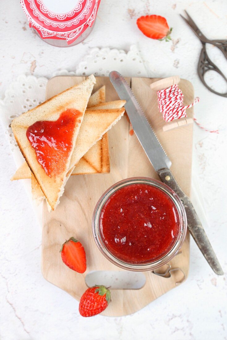 Homemade strawberry jam in a jar and on triangles of toast
