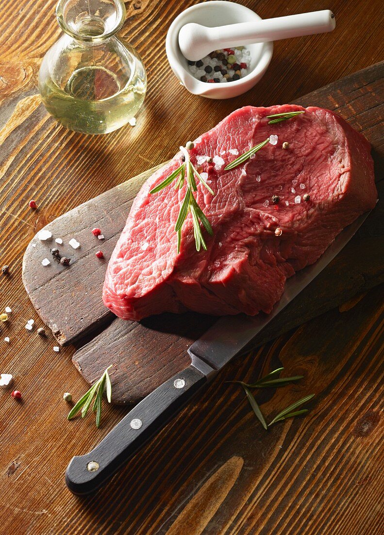 Rohes Rinderfilet (450g) auf Holzbrett mit Rosmarin und buntem Pfeffer