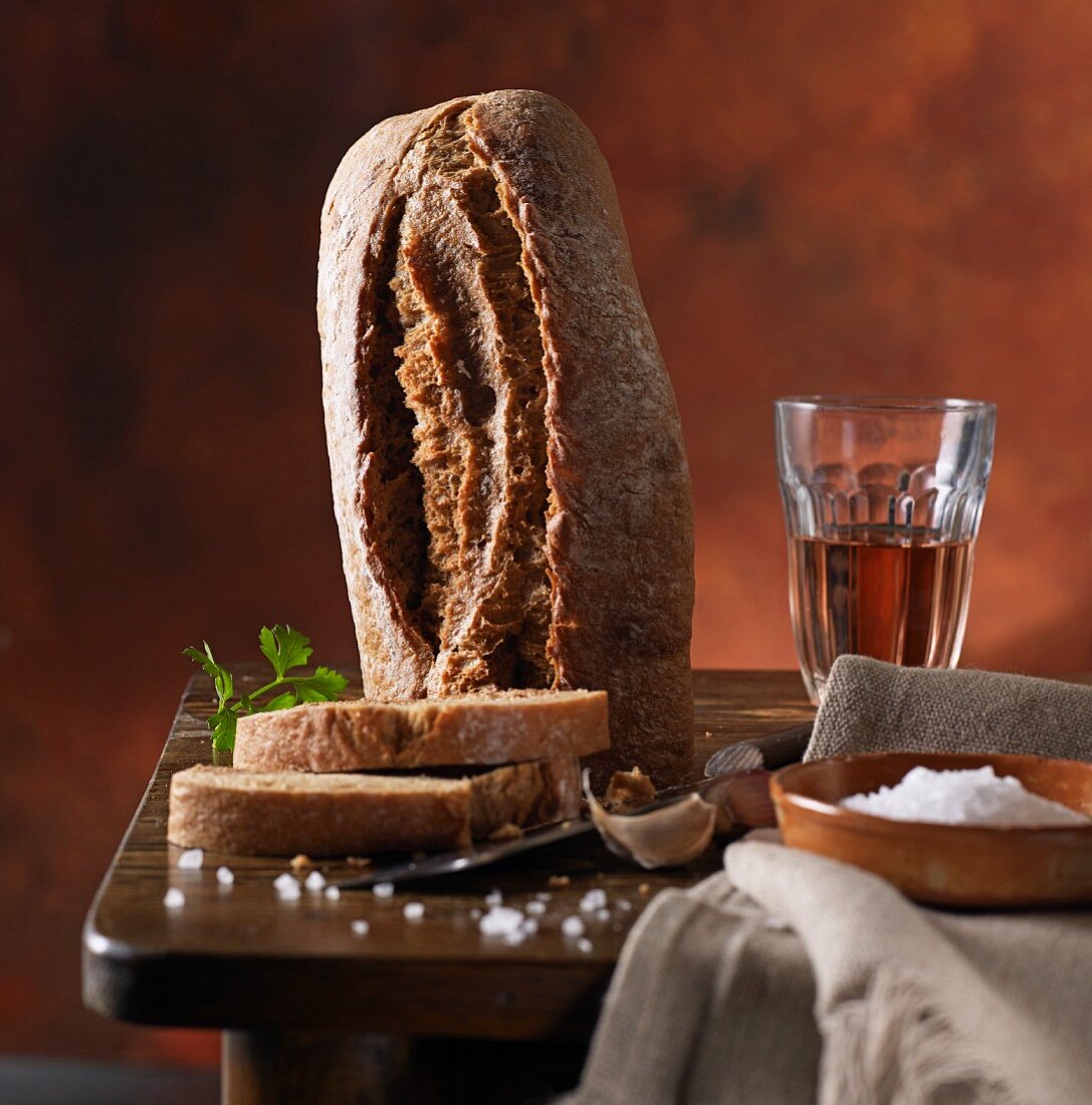 A rustic loaf of bread with coarse salt and wine on a wooden table
