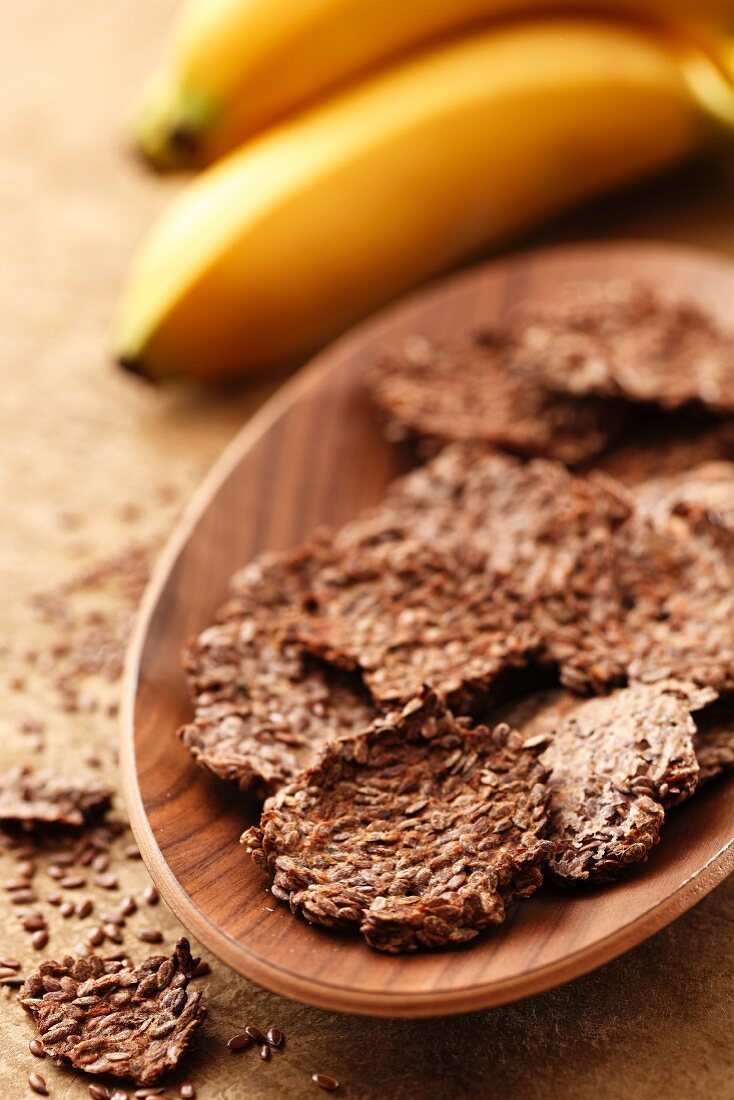 Flax seed and banana biscuits in a wooden bowl with bananas in the background