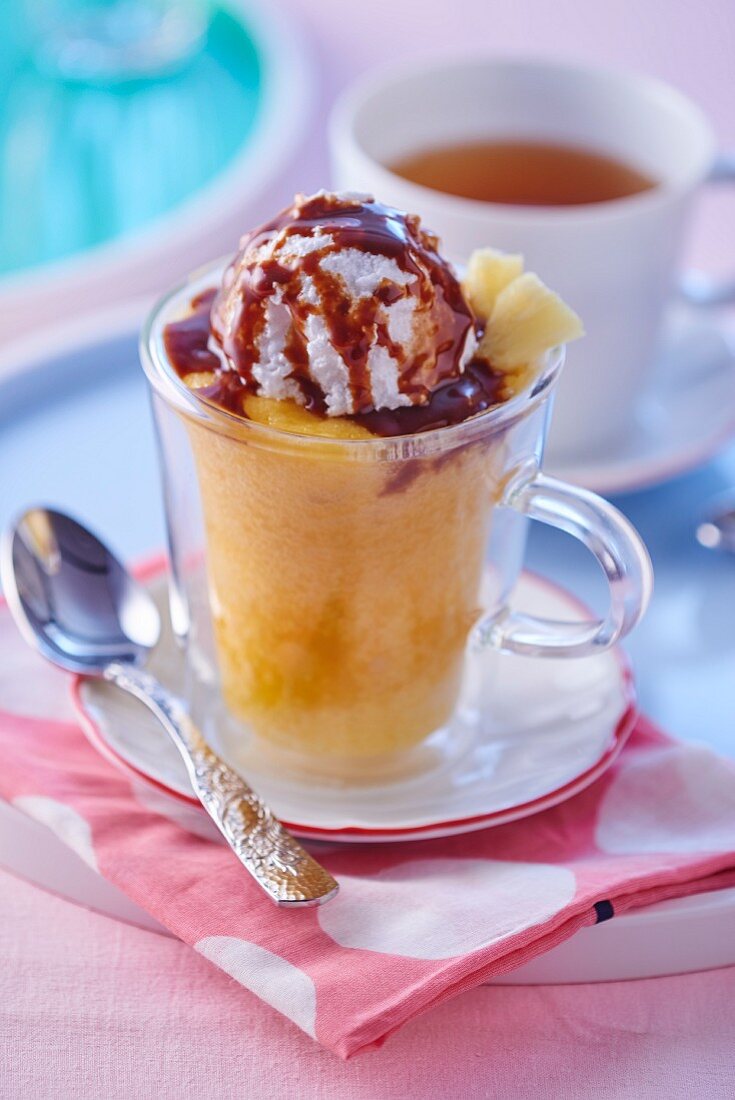 A mug cake with pineapple, a scoop of ice cream and chocolate sauce