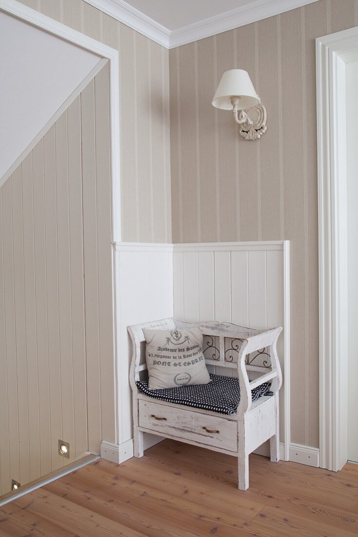 Printed vintage-style cushion on small bench against wall panelling on landing at head of staircase