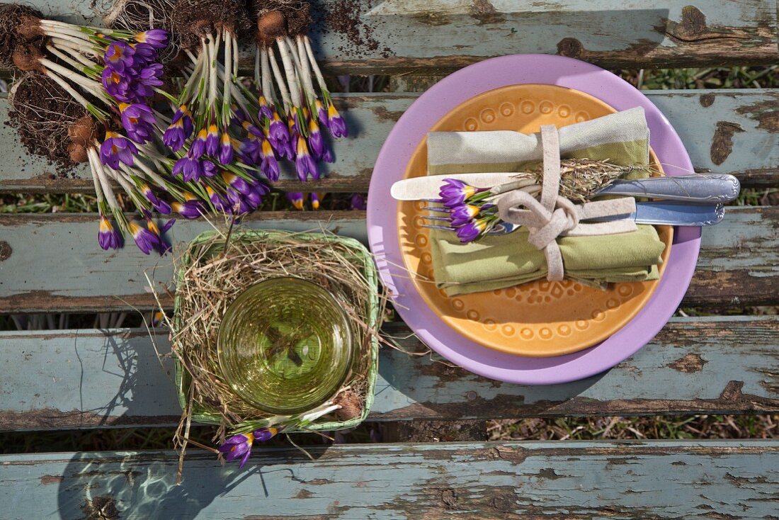 Place setting with linen napkin, cutlery and purple crocuses on wooden surface