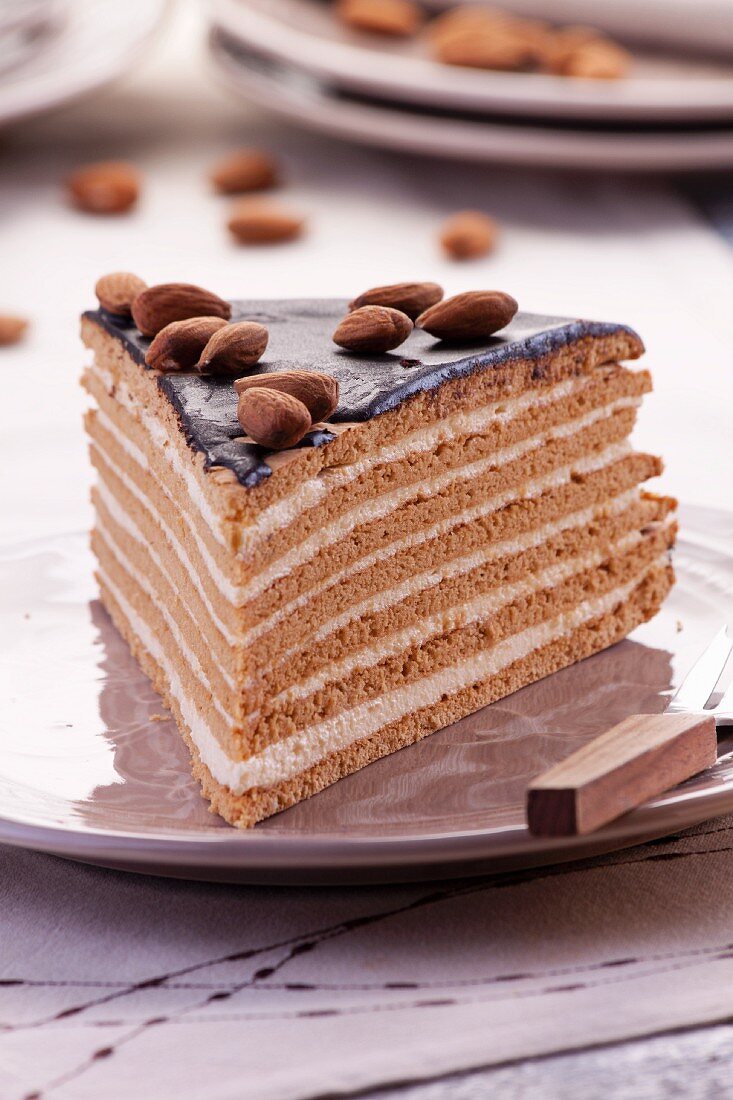 A slice of layered chocolate, toffee and almond cream cake decorated with almonds