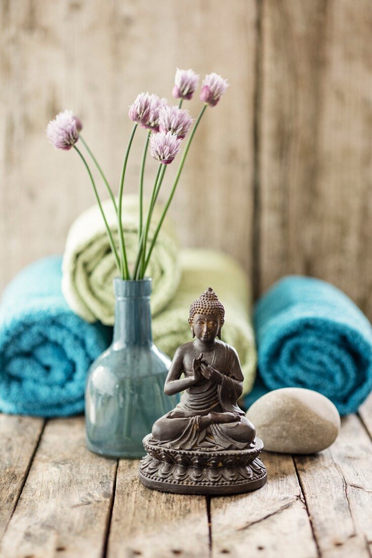 Buddha statue, vase of chive flowers, pebble and towels