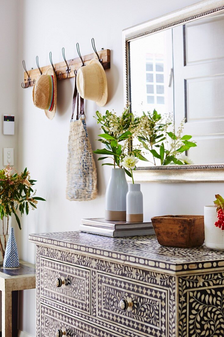 Artful ethno chest of drawers with inlays in the hallway and elegant wall mirror next to rustic coat hooks