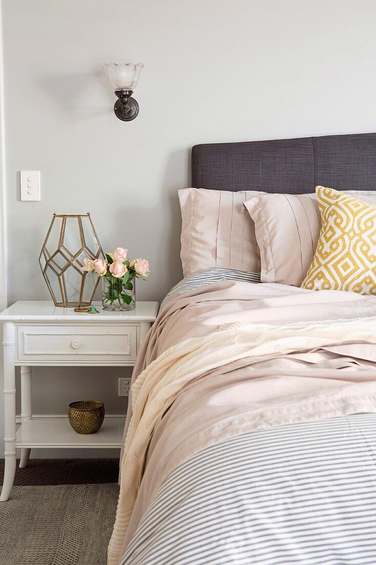 Feminine bedroom with white bedside table and bouquet of roses